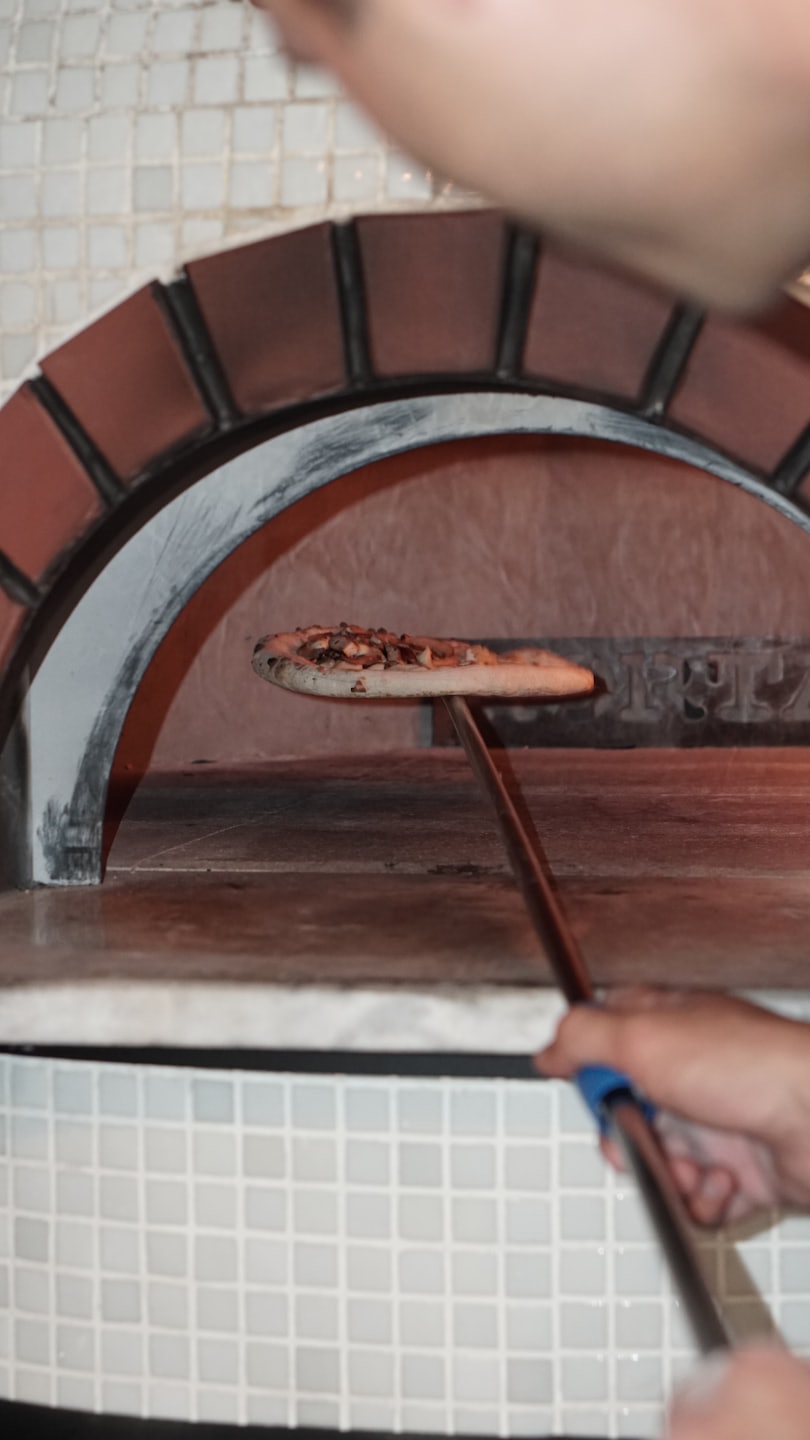Ruky zasúvajú pizzu do horúcej tehlovej pece.